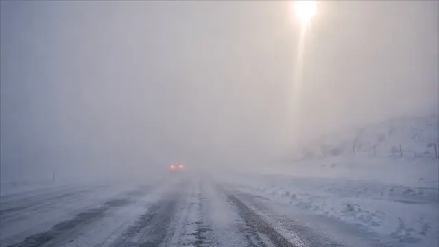 Coche en carretera nevada con niebla densa y sol