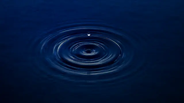 Gota de agua creando ondas en superficie azul profunda