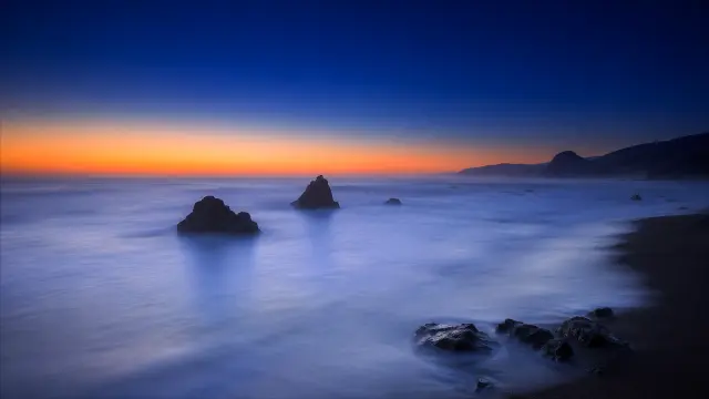 Atardecer en la costa con rocas y cielo azul
