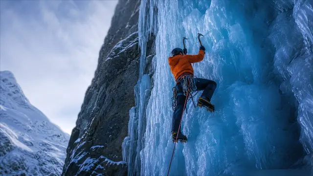Alpinista escalando pared de hielo azul en montaña nevada